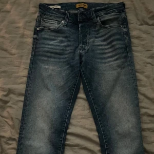 Jack & Jones Glenn jeans  - Snygga blå jeans från Jack & Jones med en klassisk femficksdesign. De har en lätt tvättad look och är perfekta för en avslappnad stil. Jeansen har en knappgylf och bälteshällor.       W 28 L 32 pris ej hugget i sten