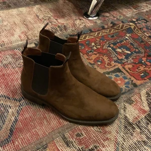 Bruna mocka Chelsea boots från H&M - Snygga bruna Chelsea boots i mocka från H&M. De har en klassisk design med elastiska paneler på sidorna för enkel på- och avtagning. Perfekta för en stilren look.