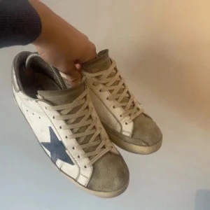 Beige sneakers med blå stjärna - Snygga beige sneakers med en iögonfallande blå stjärna på sidan. Skorna har snörning och en klassisk design som passar perfekt till en avslappnad stil.