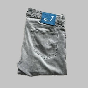 Grå jeans från Jacob Cohën - Snygga grå jeans från Jacob Cohën, handgjorda i Italien. Tillverkade av exklusiva tyger med en blandning av bomull och elastan för extra komfort. Perfekta för en stilren look.  Två pytte små defekter som inte man störa sig på, kolla de två sista bilderna