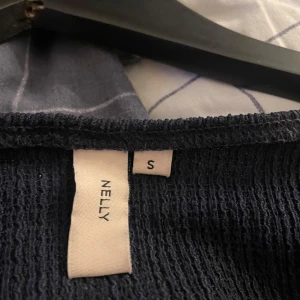 Svart v-ringad topp från Nelly - Snygg svart v-ringad topp från Nelly med långa ärmar och knyte där bak eller där fram om man skulle vilja