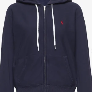 Mörkblå hoodie med dragkedja från Ralph Lauren - Säljer en stilren mörkblå hoodie från Ralph Lauren med dragkedja och vit snörning i huvan som tyvärr har lossnat, i storlek xs! Bra skick och använd några gånger som jag säljer pga att den börjat bli för liten!💗