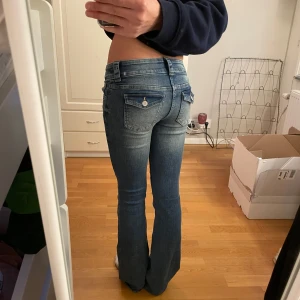 Blå bootcut jeans - Snygga blå bootcut jeans med låg midja och dubbla knappar fram. Perfekta för en avslappnad stil med en touch av retro. De har en klassisk femficksdesign och en lätt tvättad look.