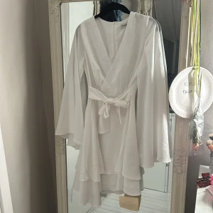 Adoore student klänning - Adoore Alexandra asymmetric dress white. Storlek 34. Perfekt till student. Jag på bild är 159. Endast provat, lapp kvar. Har tyvärr råkat göra en sminkfläck på insidan av klänningen. Något som aldrig kommer att synas när den används. Men ändå så att du som köper är medveten.  Går säkert bort i tvätten. Rosetten är lika fin fram som bak finns inga rätt o fel.