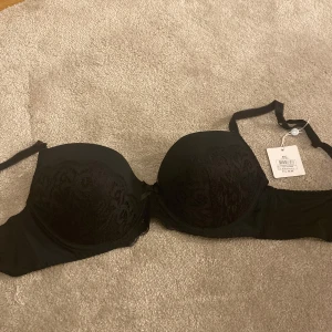 Svart spets-bh - Elegant svart bh med spetsdetaljer och justerbara axelband. Perfekt för en stilren look med en touch av lyx. Kuporna har en vacker spetsdesign som ger en feminin känsla. OBS HELT NY OCH OANVÄND, köptes i fel storlek.