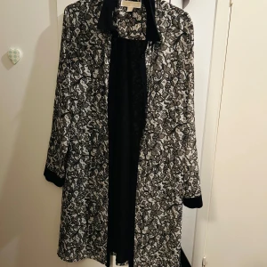 Långärmad skjortklänning från MK - Snygg långärmad klänning från Michael Kors i svart och vit med ett unikt mönster. Perfekt för att sticka ut med stil. Klänningen har en elegant design med en klassisk krage och långa ärmar.