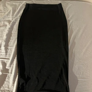 Svart kjol från NLY Trend - Snygg svart långkjol från NLY Trend i en stilren design. Kjolen har en tight passform som framhäver figuren och är perfekt för olika tillfällen. Tillverkad i ett mjukt och bekvämt material, lite glansigt material. 