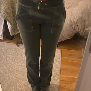 Gröna mjukisbyxor från Juicy Couture - Snygga gröna mjukisbyxor från Juicy Couture med bred resår i midjan och snörning. Byxorna har praktiska fickor fram och bak med knappar. Perfekta för en avslappnad stil💞