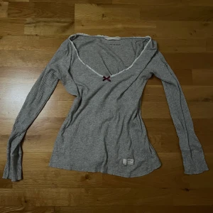 Grå ribbad tröja från Odd Molly - Säljer en grå ribbad tröja från Odd Molly med en söt rosett framtill. Tröjan har långa ärmar och en v-ringad halslinje med spetsdetaljer. Den är i fint skick och har inga tydliga tecken på användning. 