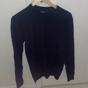Mörkblå stickad tröja från J.Lindeberg - Säljer en stilren mörkblå stickad tröja från J.Lindeberg. Perfekt för kyliga dagar med sin mjuka och bekväma passform. Tröjan har långa ärmar och en klassisk rund halsringning. 