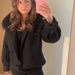 Svart kappa med knappar - Säljer en snygg svart kappa med stora knappar och långa ärmar. Den har en klassisk stil och är perfekt för höst och vinter. Jackan är i mycket bra skick och passar både till vardags och fest. Perfekt för att hålla sig varm och stilren! En liten knapp som håller fast pälsen har gått av men inhet man alls tänker på. Skriv gärna för fler frågor och funderingar❤️