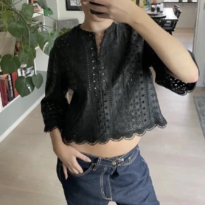 Svart blus med broderade detaljer - Säljer en snygg svart blus med broderade detaljer och trekvartsärmar. Blusen har en fin scalloped kant och knappar framtill. Perfekt för både vardag och fest!