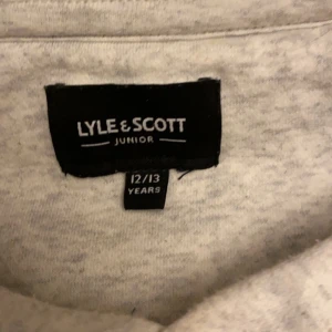 Grå hoodie från Lyle & Scott Junior - Säljer en supermjuk och bekväm grå hoodie från Lyle & Scott Junior. Den har en klassisk känguruficka och en liten gul logga på bröstet. Perfekt för både skola och fritid! 🐥passar båda yngre och up till 17 beroronde på hur man vill den ska sitta 