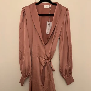 Rosa omlottklänning från VILA - Säljer en superfin rosa omlottklänning från VILA i storlek 36. Klänningen har långa ärmar och ett knytband i midjan för en snygg passform. Perfekt för både vardag och fest! Helt my och aldrig använd 