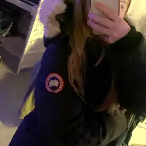 Säljer en svart parkajacka från Canada Goose i mycket bra skick. Jackan har en mysig pälsfodrad huva och är perfekt för kalla vinterdagar. Den är långärmad och har en klassisk passform. Perfekt för både vardag och vinteräventyr!