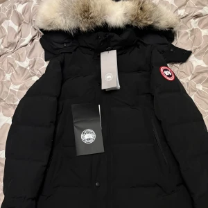 Svart dunjacka från Canada Goose - Säljer en svart Canada Goose dunjacka i storlek L. Jackan är i nytt skick med etiketter kvar. Den har en stor, fluffig päls på huvan och är perfekt för kalla vinterdagar. Jackan har en klassisk design med lång ärm och är supervarm. Perfekt för dig som vill hålla stilen i vinter! Har fler bilder men fick bara lägga in 5 så skriv privat om ni har några funderingar/ vill ha fler bilder. Jackan och pälsen är inpackade i olika påsar och allt skickas i en stor Canada goose bag. 