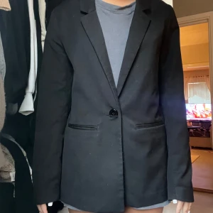 Svart kavaj från H&M - Snygg svart kavaj från H&M i bra skick. Perfekt för både vardag och fest! Den har en klassisk design med en knapp framtill och långa ärmar. Passar till alla tillfällen där du vill se lite extra stilren ut. 🖤