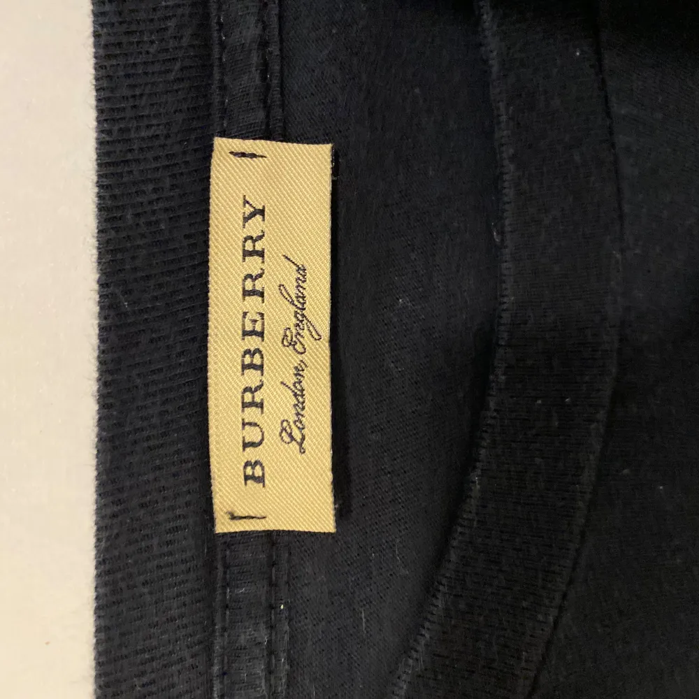 Säljer en snygg svart t-shirt från Burberry med vit text 'BURBERRY LONDON ENGLAND' på framsidan. Den är i bra skick och perfekt för en casual look. Passar både till vardags och fest. Den har två små fläckar på  r och e men inget som märks av. T-shirts.