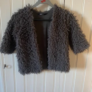 Grå pälsjacka från Gina Tricot - Säljer en supercool grå pälsjacka från Gina Tricot i storlek XXS. Jackan har en fluffig och mysig look med trekvartsärmar, perfekt för att ge din outfit en extra edge. Den är i mycket bra skick och passar perfekt för höst och vår.
