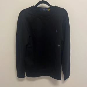 Svart tröja från Polo Ralph Lauren - Säljer en stilren svart tröja från Polo Ralph Lauren. Den har en liten blå logga på bröstet och är perfekt för både vardag och fest. Tröjan är i mycket bra skick och har långa ärmar. Passar perfekt till höst och vinter.