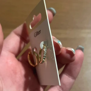 Guldiga örhängen från Glitter - Snygga guldiga örhängen från Glitter med strass. Perfekta för att ge lite extra bling till din outfit. De är nya och oanvända, fortfarande på originalkortet. Passar både till vardag och fest! 50kr+frakt