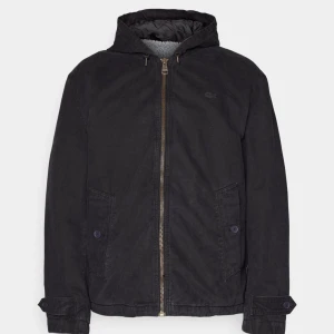 Svart jacka från Lacoste - Säljer en snygg svart jacka från Lacoste. Den har en dragkedja framtill och en huva för extra skydd mot väder. Jackan är perfekt för höst och vår, med långa ärmar och en stilren design. Passar både till vardags och lite finare tillfällen.