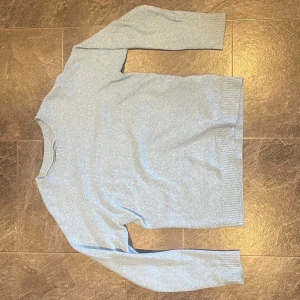 Ljusblå stickad tröja - Säljer en superfin ljusblå stickad tröja som är perfekt för kyliga dagar. Den har en klassisk rund hals och långa ärmar. Tröjan är i mycket bra skick och känns riktigt mjuk och skön. Perfekt för både vardag och mysiga hemmakvällar!