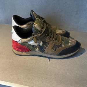 Valentino Garavani sneakers i camouflage - Snygga Valentino Garavani sneakers i camouflage med coola röda detaljer och vit häl. Skorna har en unik design med en bekväm sula. Perfekta för att sticka ut i mängden nu till vintern! Skorna är i storlek 39 men passar storlek 40.