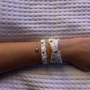 Vitt armband med nitar - Snyggt vitt armband med guldiga nitar och fransiga kanter. Perfekt för att ge en edgy touch till din outfit. Armbandet är justerbart och passar de flesta handleder. Kombinera med andra smycken för en unik stil!