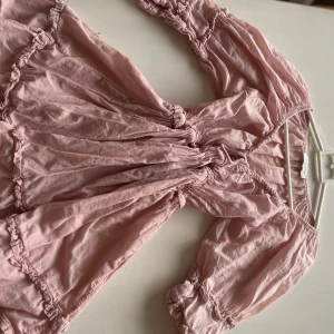 Ljusrosa klänning från Monton - Söt ljusrosa klänning från Monton med volangdetaljer. Den har en luftig passform och trekvartsärmar, perfekt för vår och sommar. Materialet känns lätt och bekvämt, vilket gör den idealisk för både vardag och festliga tillfällen. 