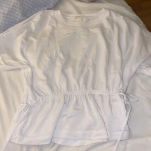 T-shirt med knytning i midjan  - Hej💕 Just nu säljer jag denna populära och slutsålda T-shirt med knytning i midjan ifrån H&M. T-shirten är i Mycket bra skick och är super fint både att ha vardagligt och uppklätt, hör gärna av er vid fler frågor eller bilder!🫶🏻Säljer pga inte min stil längre
