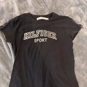 Svart Hilfiger t-shirt - Svart Hilfiger t-shirt med paljett text! Det är i stl L men den sitter mer som en S/M