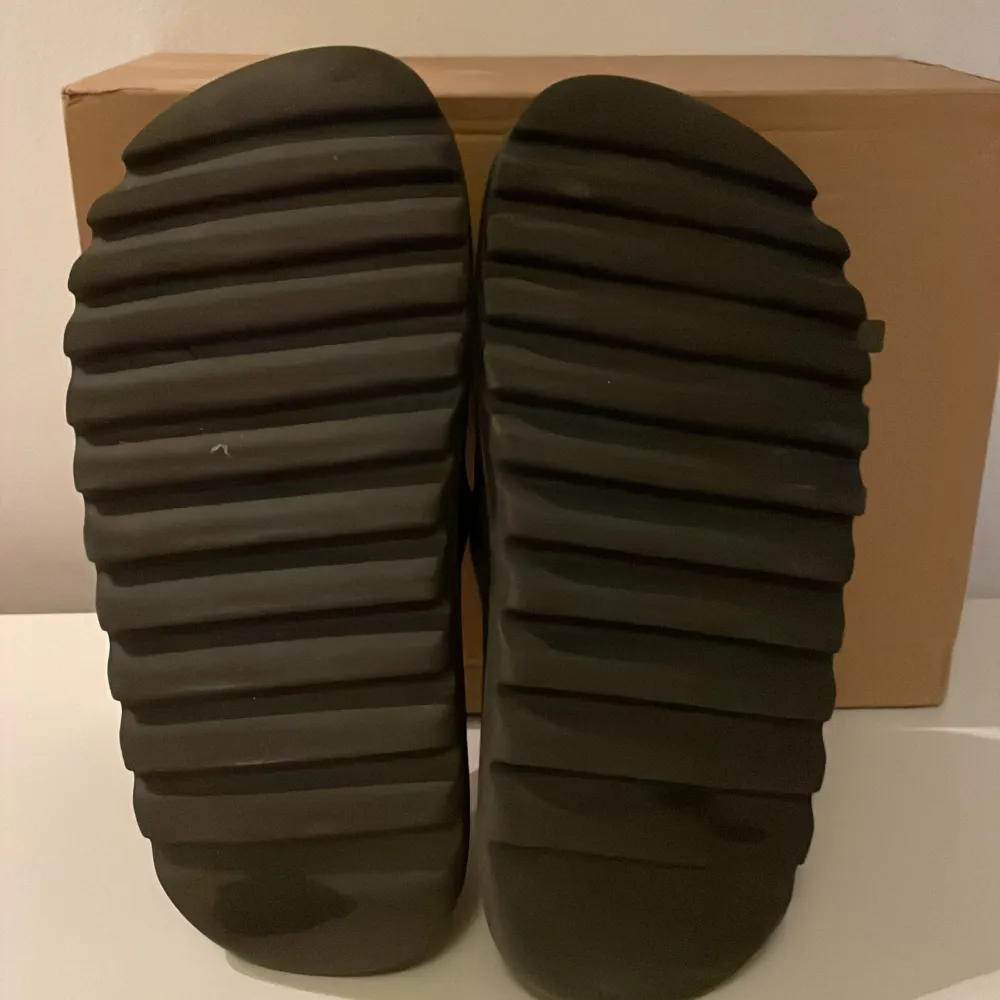 Säljer ett par yeezy slides i färgen onyx i bra skick men liten skada under sulan. De är perfekta för sommarens alla äventyr eller bara att glida runt hemma. Liten i storleken, har vanligtvis 42 men i dessa 44,5. Kommer i originalbox . Perfekta för en avslappnad stil!. Skor.