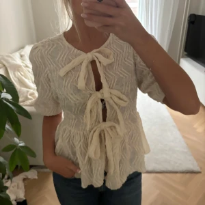 Vit blus med knytband - Säljer en superfin vit blus med korta ärmar och knytband framtill. Den har ett snyggt texturerat mönster och en luftig passform, perfekt för vår och sommar. Blusen är i mycket bra skick och passar både till vardags och fest.❤️