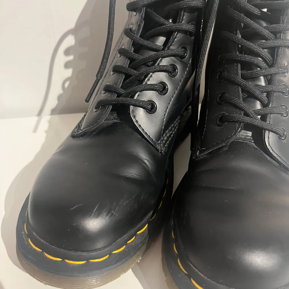 Säljer ett par klassiska svarta Dr. Martens boots i skinn med den ikoniska gula sömmen. De har snörning och en robust sula som är perfekt för höst och vinter. Kängorna har endast använts enstaka gånger, men har en liten defekt fram på skon (visat på bilden). Hund finns i huset.. Skor.