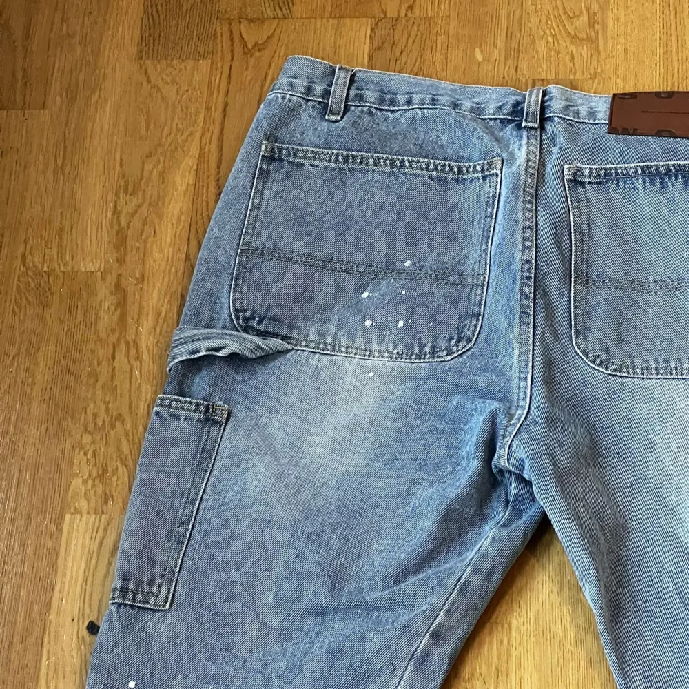 Säljer ett par blå jeans med coola fickor på sidorna. De har en avslappnad stil med slitna detaljer och lite färgstänk för en unik look. Perfekta för en casual outfit eller en dag ute. Passar bra till sneakers eller kängor.. Jeans & Byxor.