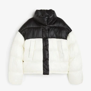 Svart och vit pufferjacka - Säljer en snygg svart och vit pufferjacka i syntetmaterial. Jackan har en hög krage och stängs med både dragkedja och knappar. Perfekt för kalla dagar med sin varma och vadderade design. Den har en cool kontrast mellan svart och vitt som gör den unik. Passar perfekt för vintern!🤍🖤