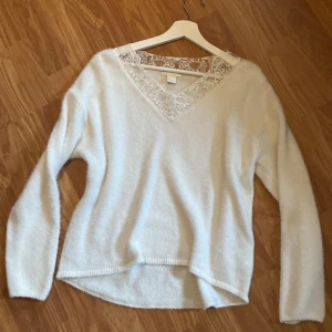 Vit stickad tröja med spetsdetaljer - Säljer en superfin vit stickad tröja med v-ringning och spetsdetaljer vid halsen. Perfekt för både höst och vinter, den är både mysig och stilren. Tröjan har långa ärmar och är i mycket bra skick.