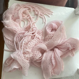 Rosa stickad halsduk - Superfin rosa stickad halsduk i ett luftigt och mjukt material. Perfekt för att hålla sig varm under kyliga dagar. Den har fransar i ändarna som ger en extra touch av stil. Passar perfekt till både höst och vinteroutfits!