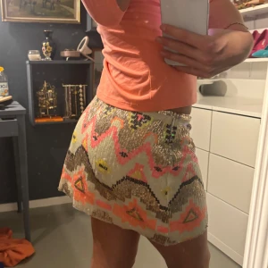 Glittrig kjol med mönster - Säljer en superfin glittrig kortkjol med färgglatt mönster i rosa, beige och svart. Perfekt för festliga tillfällen! Kjolen har en tight passform och är täckt med paljetter som ger en extra glamorös touch. Den är i mycket bra skick och redo att bäras på nästa party! ✨