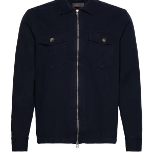 Mörkblå overshirt med dragkedja - Säljer en stilren mörkblå overshirt med dragkedja framtill. Den har två bröstfickor med knappar och en klassisk krage. Perfekt för lager-på-lager under höst och vår. Passar både till vardags och lite mer uppklädda tillfällen. Helt oanvänd. Nypris 2800