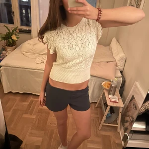 Vit stickad topp med volangdetaljer - Säljer en superfin vit stickad topp med volangdetaljer på ärmarna. Den är perfekt för sommaren och har en tight passform som framhäver figuren. Toppen är i mycket bra skick och passar både till vardags och fest. Perfekt att matcha med jeans eller kjol!
