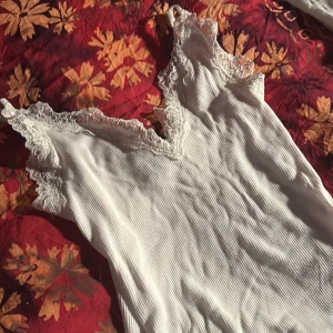 Vit ribbad topp från Amisu - Säljer en superfin vit ribbad topp från Amisu i storlek XXS. Den har vacker spetsdetalj vid halsringningen och ärmlös design. Perfekt för sommardagar eller som ett lager under en kofta. Toppen är i mycket bra skick och redo för en ny ägare!