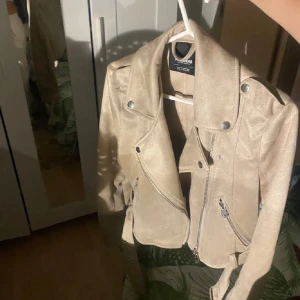 Beige mockajacka från Zara - Säljer en snygg beige mockajacka från pill and bear. Den har en cool bikerstil med dragkedja och knappar. Perfekt för höst och vår! Jackan är i bra skick och passar till både vardag och fest.