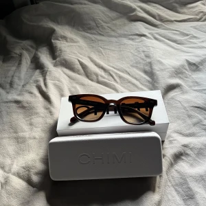 Bruna solglasögon från CHIMI - Säljer ett par snygga bruna solglasögon från CHIMI 02. De har en klassisk rund form och kommer med ett stilrent fodral. Perfekta för soliga dagar och ger en cool look. Glasögonen är i mycket bra skick och redo för nya äventyr!