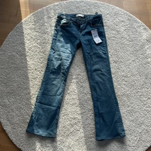 Blå bootcut jeans från Zara - Säljer ett par snygga blå bootcut jeans från Zara i storlek 38. De är lågmidjade och har en slim passform med utsvängda ben. Perfekta för en avslappnad men stilren look. Helt nya med prislapp kvar!