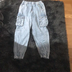 Ljusa cargopants - Säljer ett par ljusa cargopants i bra skick. De har elastisk midja och muddar vid bensluten för en bekväm passform. Byxorna har flera praktiska fickor med knappar på sidorna, perfekt för en avslappnad stil. Perfekta för vår och sommar!