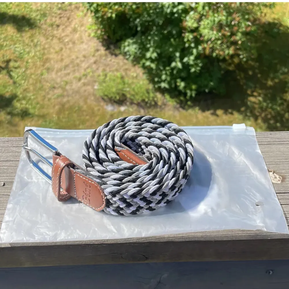 Säljer ett snyggt flätat bälte från Béné i svart, grått och vitt. Bältet har en stilren design med ett brunt läderparti och en silverfärgad spänne. Perfekt för att ge din outfit en cool touch! Passar både till vardags och fest. 🖤🤍. Muu.