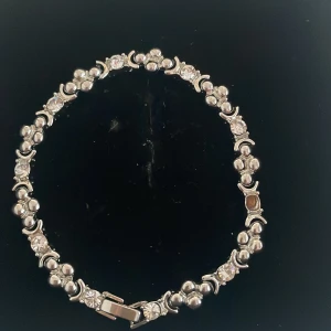 Silverfärgat armband med glittriga detaljer - Snyggt silverfärgat armband med glittriga stenar som ger en elegant touch.En sten fattas. Perfekt för festliga tillfällen eller som en fin accessoar till vardags. Armbandet har en säker låsning och en stilren design som passar de flesta stilar.