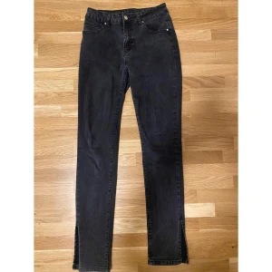 Svarta jeans med slits - Säljer ett par svarta jeans i mycket bra skick. De har en snygg slits vid bensluten som ger en unik touch. Passformen är normal och de är högmidjade.